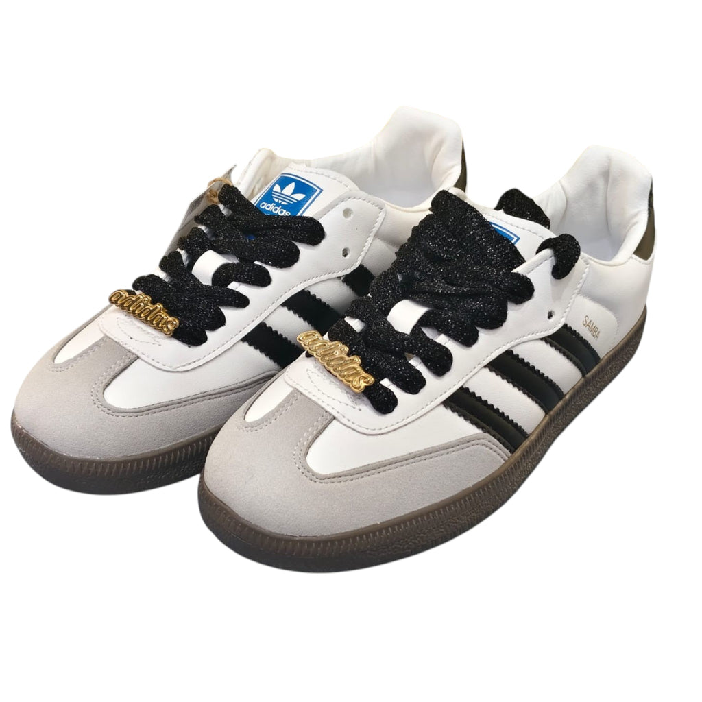 Zapatillas Adidas Samba OG de cuero blanco y ante gris con cordones negros y detalles dorados. Marca Planet Shoes Sneakers.