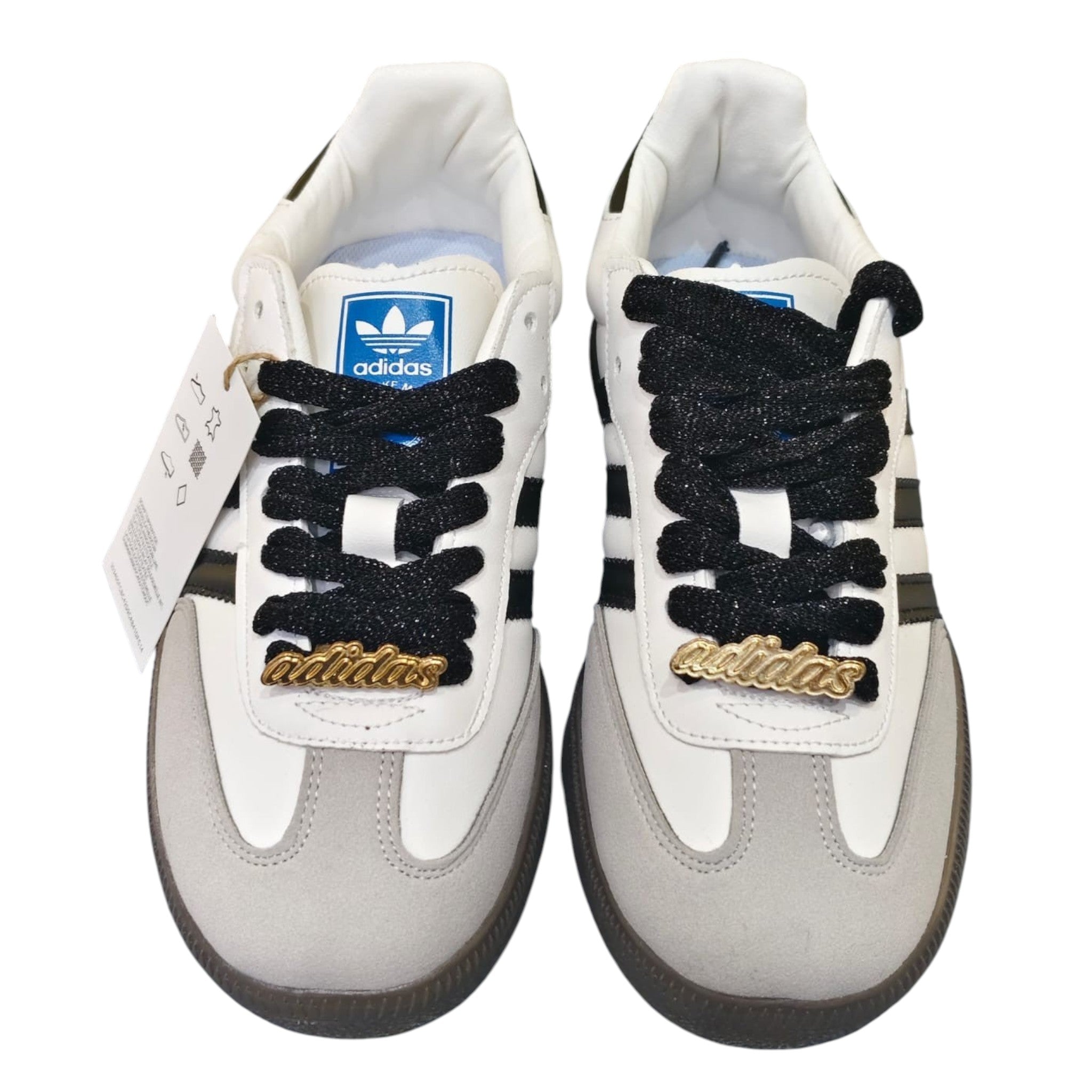 Zapatillas Adidas Samba OG de cuero blanco y ante gris con cordones negros y detalles dorados. Suela de goma marrón.
